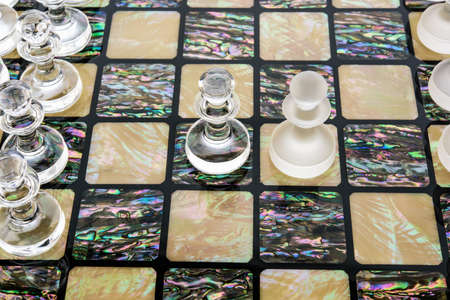 Transparent different glass chess pieces figures standing on pearl board in white. Glossy and matte...