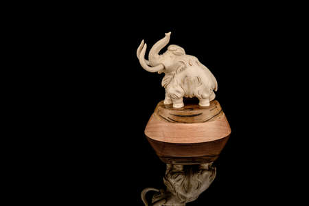 Ivory statuette of elephant mammoth on black background with reflection. carved with a gouge from old bone. authentic decorative figure for interior.の写真素材