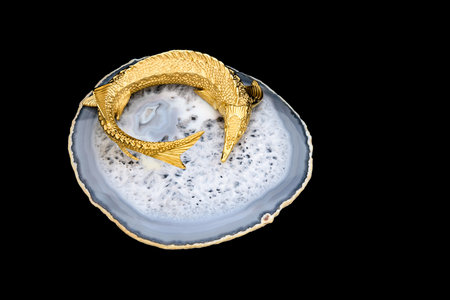 Gilded luxury crystal caviar bowl on stand made of natural quartz, carved brass fish figurine on a black background.の写真素材