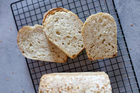 Baked Ruddy Wheat Brick Bread sourdough and slice with flax seeds on a black grid, on gray concrete...