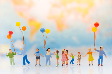 Miniature people: children hold balloons, and play together, background is map of world, using as background International day of families concept.の写真素材
