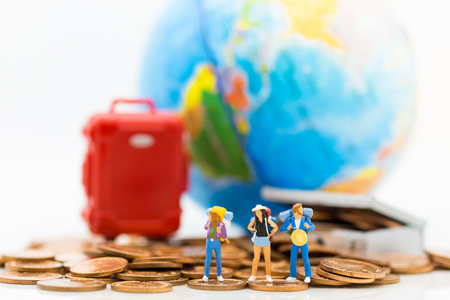 Miniature people : Travelers stand on a pile of coins and have a red suitcase, world map for background. Image use for travel, business concept.の写真素材