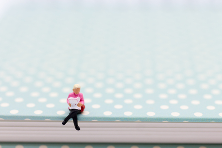 Miniature people : Businessman sitting on book and reading the newspaper. Image use for business concept.の写真素材