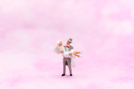 Miniature people: The groom carries the bride with pink background on wedding day. Image use for Valentine's Day concept.の写真素材