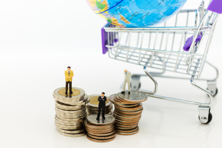 Miniature people: Businessman standing on stack of coins, shopping cart with world map for retail business. Image use for online and offline shopping, marketing place world wide, business concept.の写真素材