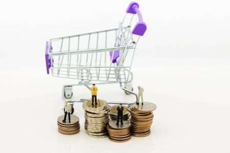 Miniature people: Businessman standing on stack of coins, shopping cart. Image use for online and offline shopping, marketing place world wide, business concept.の写真素材