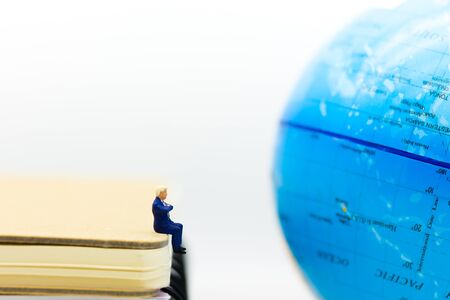 Miniature people : Businessman sitting on the book and looking to map world. Image use business concept.の写真素材