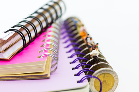 Miniature people: businessman sitting on coins reading newspaper on a big book. Image use for background education or business concept.の写真素材