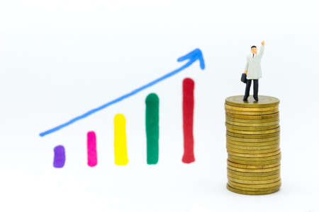 Miniature people: Businessman stand on stack of coins, display graphs, profit margins of  background. Image use for business concept.の写真素材