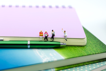 Miniature people: businessman reading newspaper on a big book. Image use for background education or business concept.の写真素材