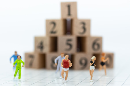 Miniature people running to stack of number wooden blockの写真素材