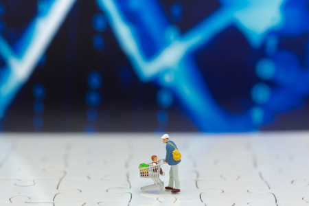 Miniature people: Shopper with shopping cart stand front of dashboard, display graphs, profit margins of retail background. Image use for market place concept.の写真素材