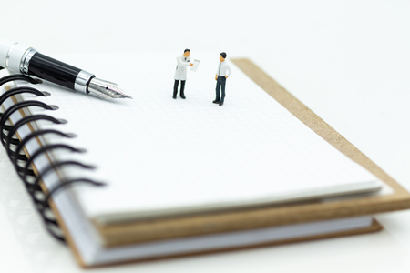 Miniature people: Businessman standing on white note and the pen. Image use for write text on paper.の写真素材