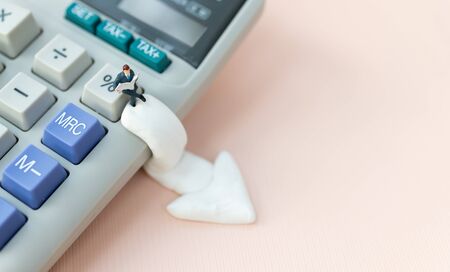 Miniature people: Businessman sitting on percent calculator with white down arrow . Image use for business banking interest, financial investment concept.の写真素材