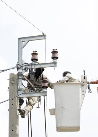Two electrician are installing new cables of high voltage that one electrician is climbing on an electric power pole, another one  is on lift bucketの写真素材