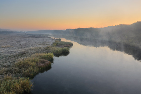 Cold morning landscape with a river. Grass covered by hoarfrost