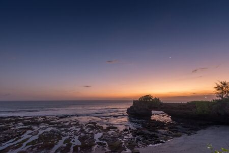 Batu Bolong Temple at dusk with moon in crescent.の写真素材