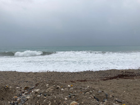 The turbulent sea storms the shore of sand mixed with pebblesの写真素材
