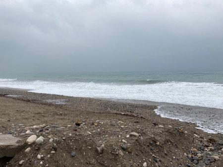 The turbulent sea storms the shore of sand mixed with pebblesの写真素材