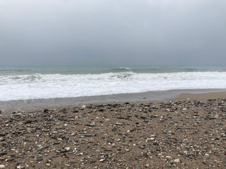 The turbulent sea storms the shore of sand mixed with pebblesの写真素材