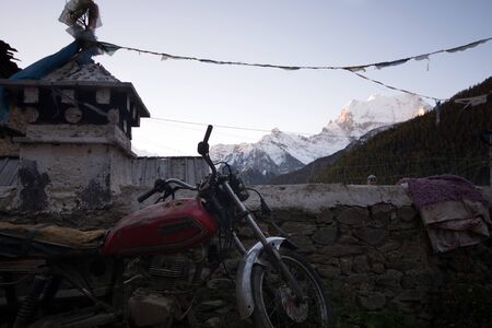 Daocheng, China - October 21, 2015: Old motorcycle leans against the wall in front of the mountain background at Daocheng, Sichuan Province, China. It has been taken on October 21, 2015.のeditorial素材