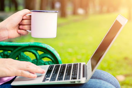 Close up hands of a woman holding a cup of coffee. girl using a laptop in the morning.の写真素材