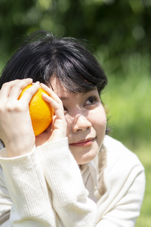 Happy asian woman holding orange in garden. Smiling people with blurry background.の写真素材