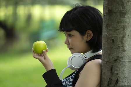 Healthy asian woman holding green apple in garden. Smiling with blurry background.の写真素材