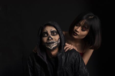 Southeast asian man with skull face makeup and woman on black background, portrait photographyの写真素材