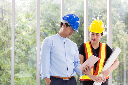 Two engineers working meeting room with a tablet. Two workers are watching construction plan. at the office. Electricians carpenter or technical operaters and labourers or moving operators.の写真素材