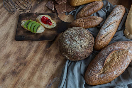 Breakfast and baked bread concept. Fresh fragrant bread and egg on wooden table. Fresh bread and coffee and wheat on wood black background. Kiwi and chocolate. Sesame seeds in the dish.の写真素材