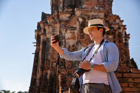 Tourists are shooting self portrait. Selfie portrait. Travel and tourism. Young caucasian male walk in the morning at temple in old city of Ayutthaya in Thailand.の写真素材
