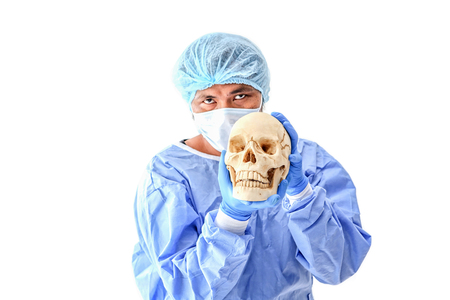 Surgeon at operating room in the hospital on white background. young doctor in uniform posing isolated in white background. The surgeon holds the skull to explain to the patient.の写真素材