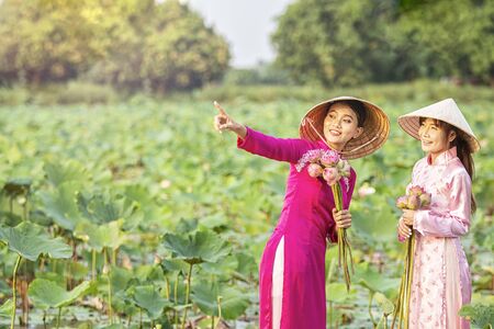 Vietnamese girls are inviting friends to look at the lotus flowers. Vietnamese dress with pink lotus flowers. Female boating on lakes harvest water lilies.の写真素材