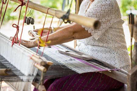 Traditional Isan Thai silk weaving. old woman hand weaving silk in traditional way at manual loom. Thailand. Selective focus.の写真素材