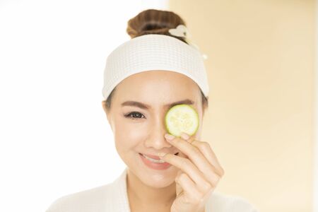 Beauty and spa condo, woman holding cucumber. Young woman with facial mask holding cucumber slices on white background.の写真素材
