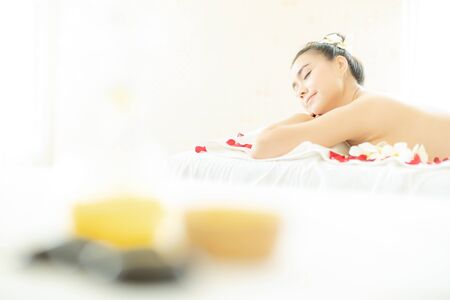 Natural cosmetics and concept. Close up of salt with massage oil and bath towel on Spa bed. Bottle of massage oil, hot stone spa and salt with woman massage in a beauty spa bed.の写真素材