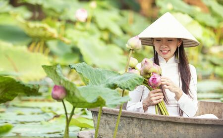 A lotus flower in the hand of a Vietnamese woman. Beautiful Vietnamese holding Pink Lotus on wooden boat in the lake vietnam.の写真素材