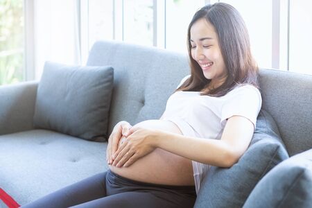 Mothers wearing wedding rings are making heart-shaped hands on their pregnant belly.の写真素材