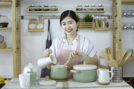 Female holding an spoon in the kitchen. Portrait of a pretty woman holding spoon made healthy food in the kitchen. Happy woman which standing in cooking place. Asian people.の写真素材