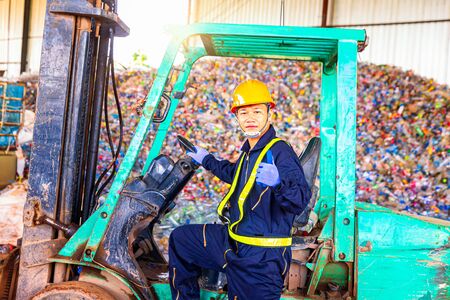Recycle employees wearing protective clothing are working in recycling plants. Foreman showing thumbs up on Forklifts in the Industrial recycle. Tipper trucks are pouring plastic bottles.の写真素材