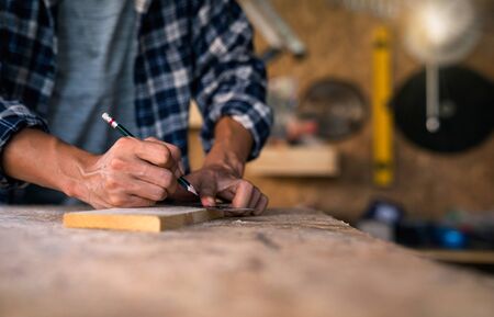 The carpenter is working on the wood cutting table in the wooden factory. Worker or Professional constructor repair workshop in wood working.の写真素材