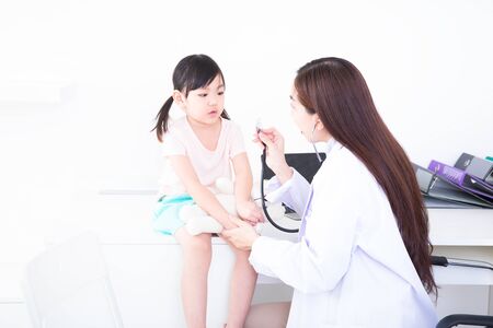 The girl is afraid of the doctor. The female doctor is using a stethoscope. The doctor examines the flu girl in a white examination room with a laptop.の写真素材