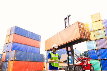 Foreman or Operator Ordering of moving containers via laptop computer. Foreman looking forward on Forklifts in the Industrial Container Cargo freight ship.の写真素材