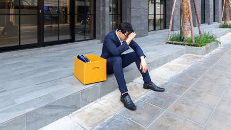 Unemployed male, The economic downturn made people unemployed, Desperate businessman sitting hopelessly on stair in central business district due to unemployment. failure, desperation.の写真素材