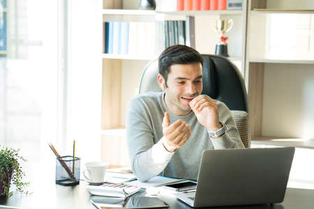 A young businessman sitting and working at home on a desk with a mobile phone and a notebook...