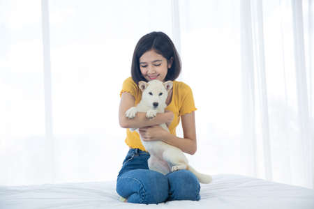 A girl hugging a Hokkaido Inu or Shiba Inu dog on a bed in a white bedroom.の写真素材