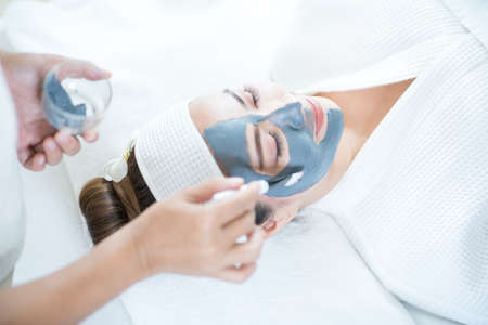 Beauty and spa condo, woman holding cucumber. Young woman with facial mask holding cucumber slices on white background. Copy space.の写真素材