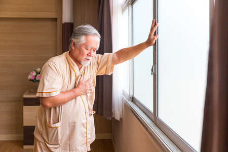 Mature man with chest pain suffering from heart attack in hospital room. Age disruption of Heart system.の写真素材