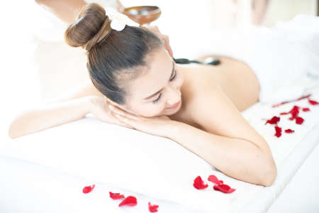 A spa masseuse is placing a hot stone on an Asian woman. Lying in a relaxing massage spa.の写真素材